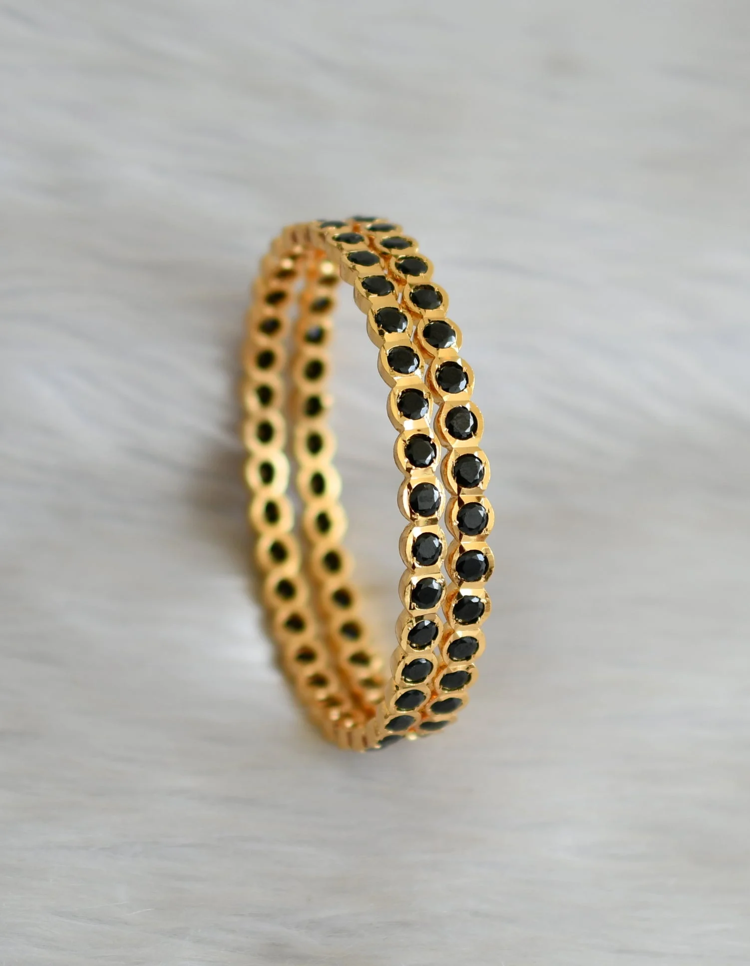 Pair of gold-tone bangles with round black accents displayed upright on pale fabric