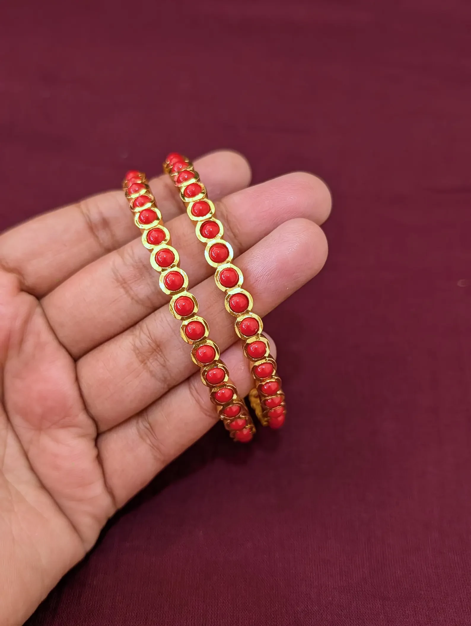 Pair of gold-tone bangles with coral-coloured round accents held across a hand