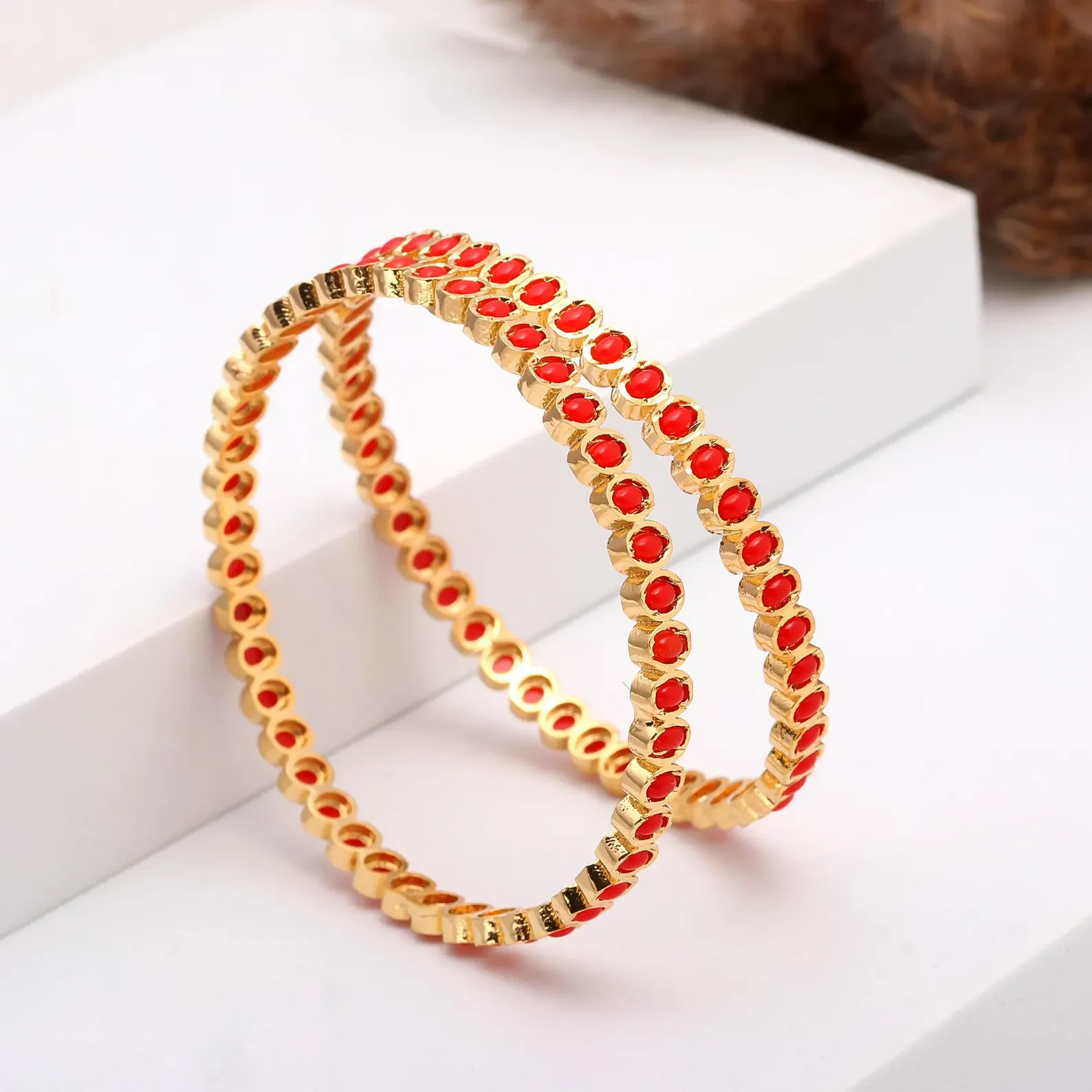 Pair of gold-tone bangles with coral-coloured round accents arranged upright on a white display