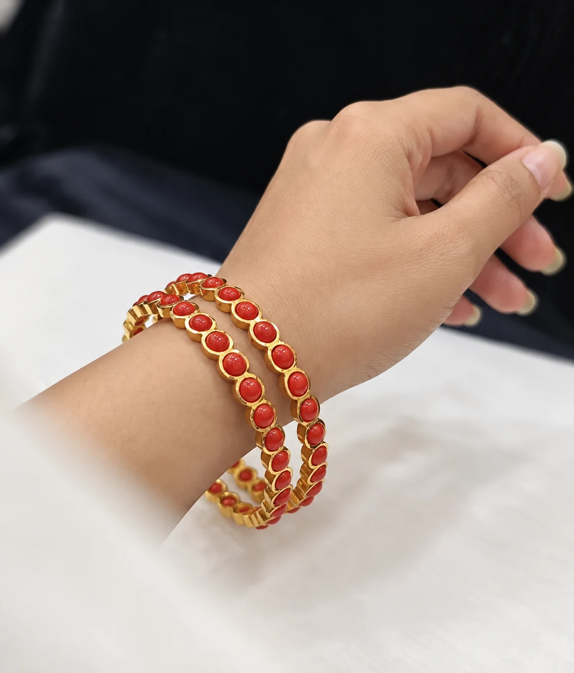 Pair of gold-tone bangles with coral-coloured round accents worn on a wrist