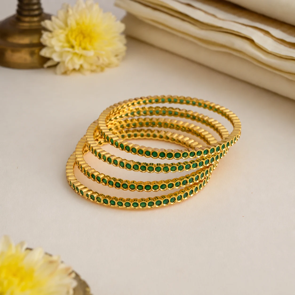 Four gold-tone bangles with round green accents arranged together on a cream tabletop