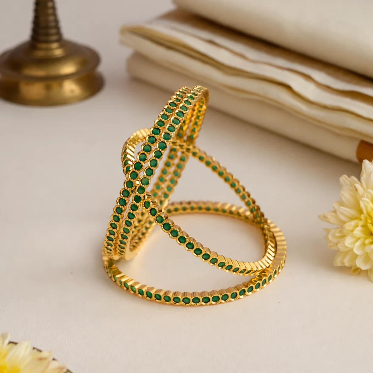 Four gold-tone bangles with round green accents arranged in a sculptural display