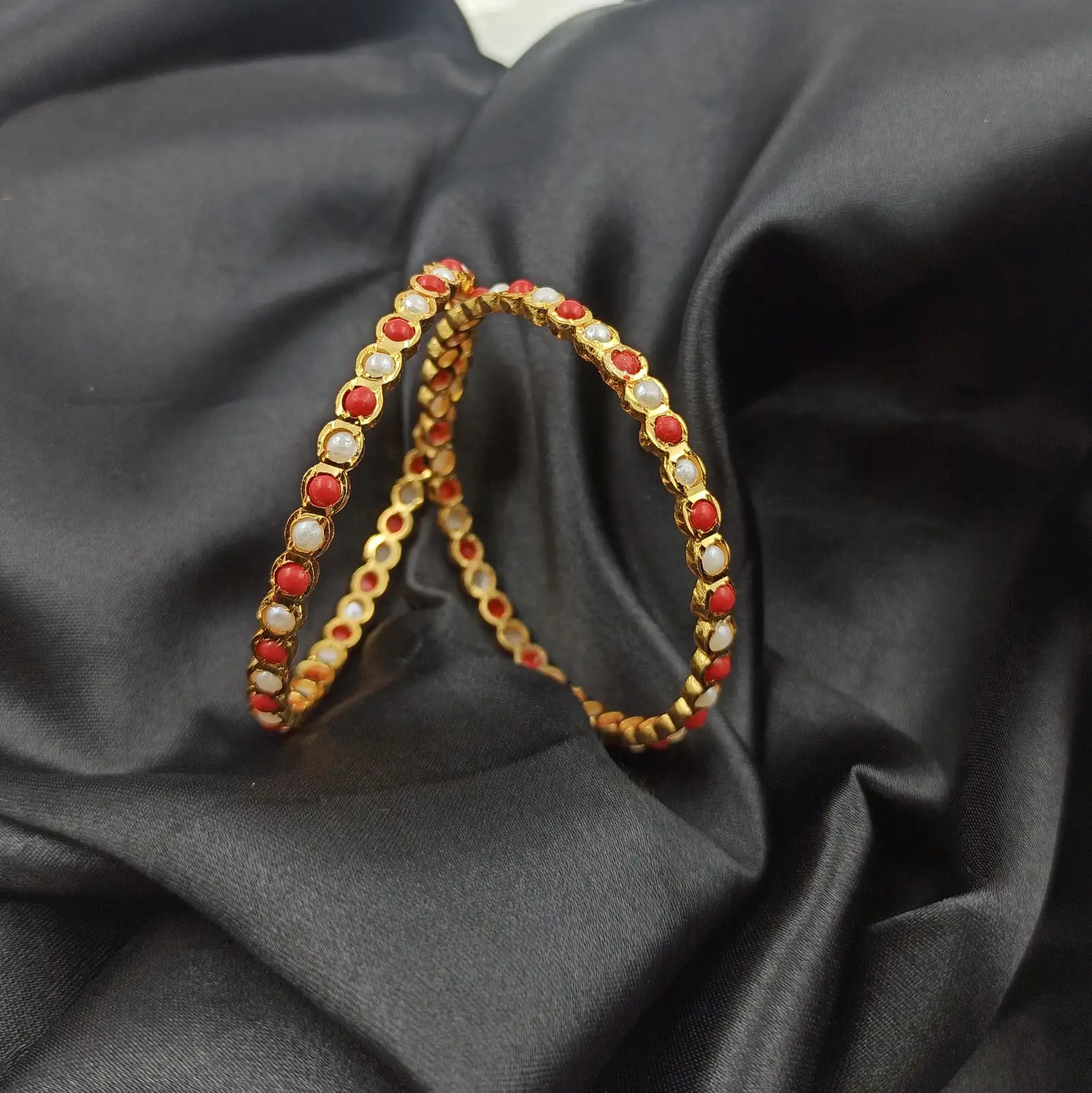 Pair of gold-tone bangles with alternating pearl-like and coral-coloured round accents arranged on black satin