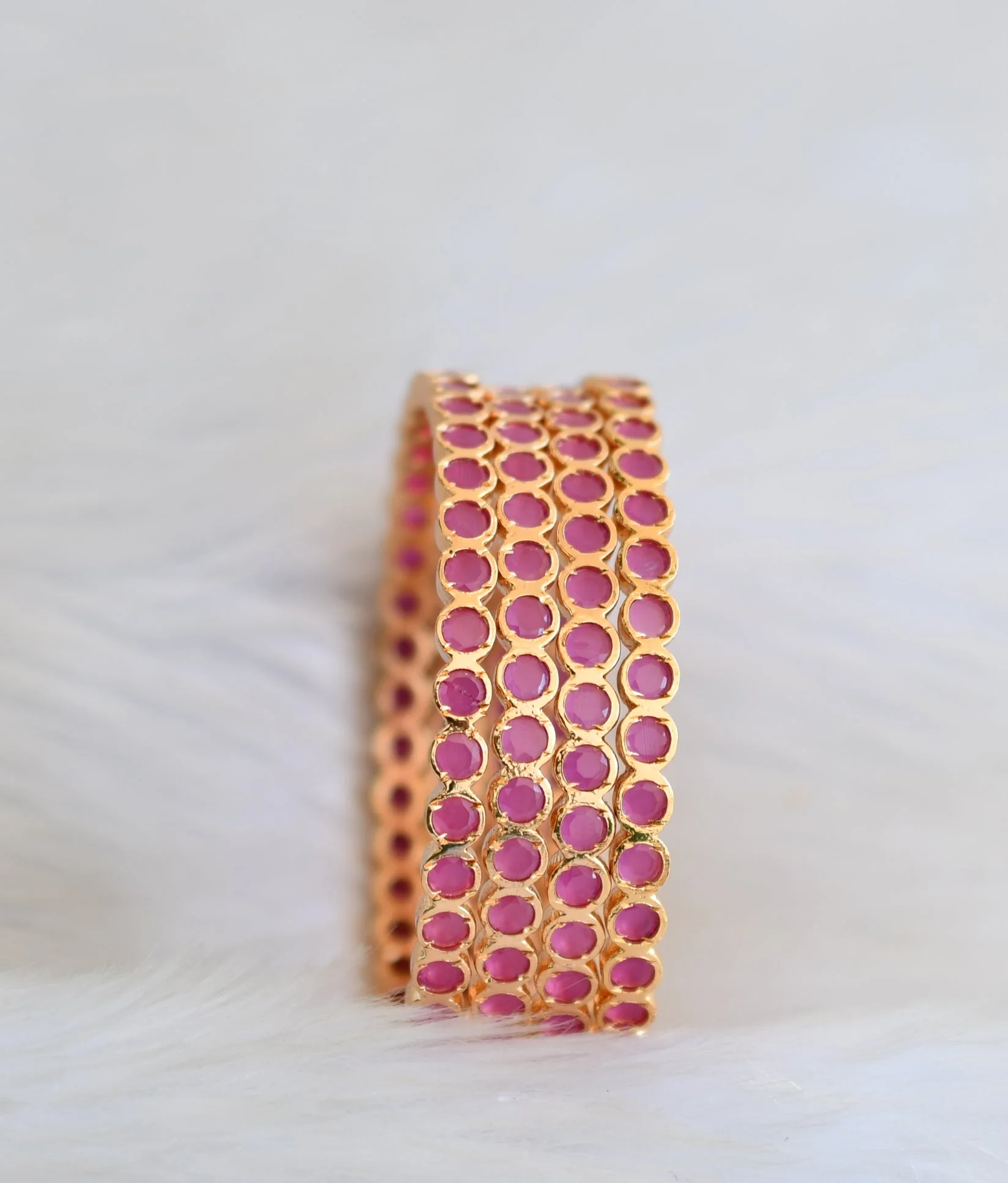Four gold-tone bangles with round ruby-coloured accents displayed upright on pale fabric