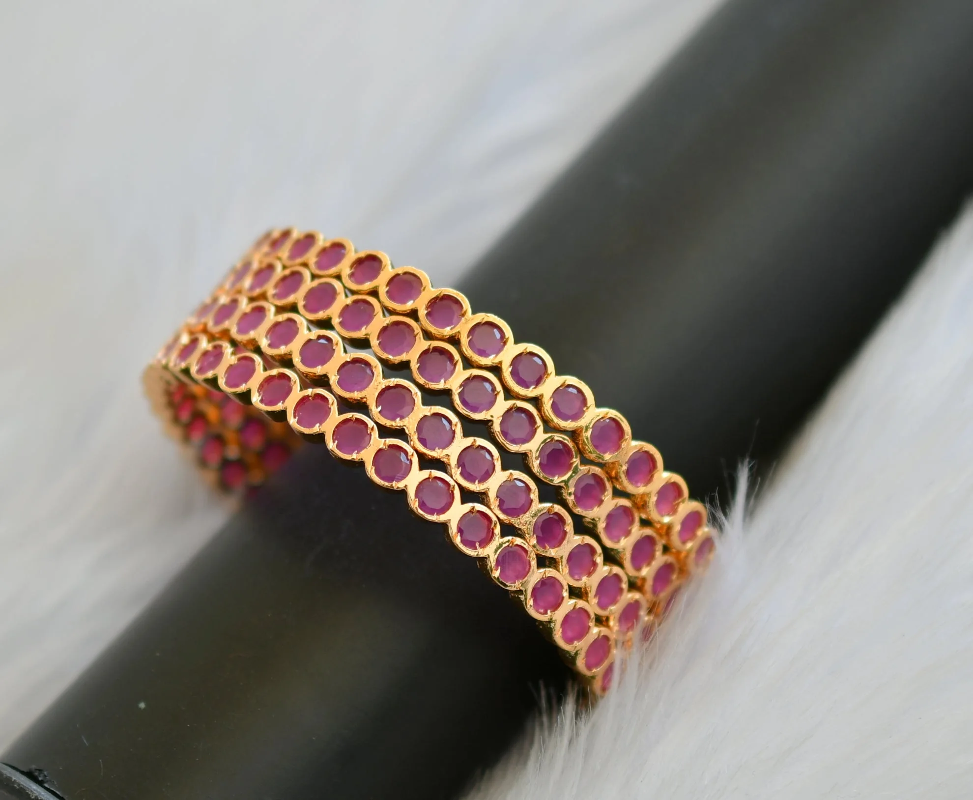 Close view of four gold-tone bangles with round ruby-coloured accents on a dark display