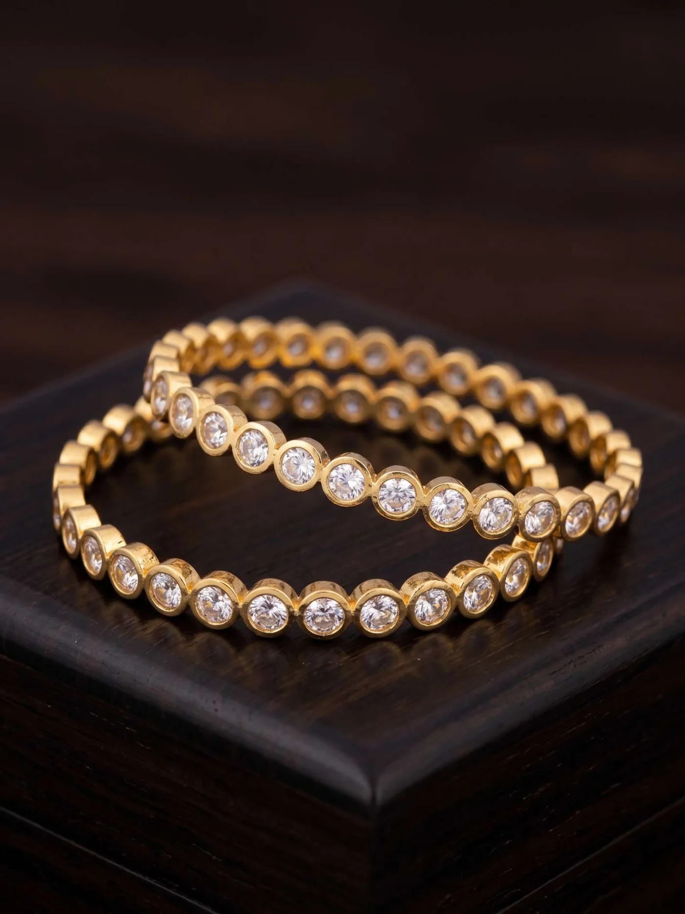 Close view of two gold-tone bangles with round white stones on a dark jewellery display