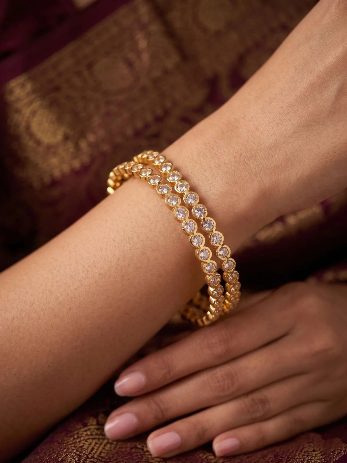 Two gold-tone white-stone bangles worn together against a maroon outfit